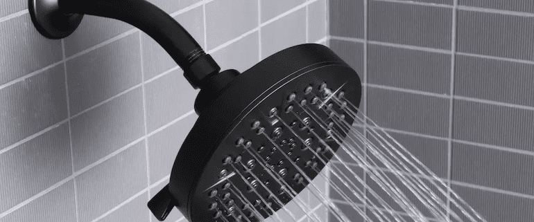 Showerhead spraying water in tiled bathroom.